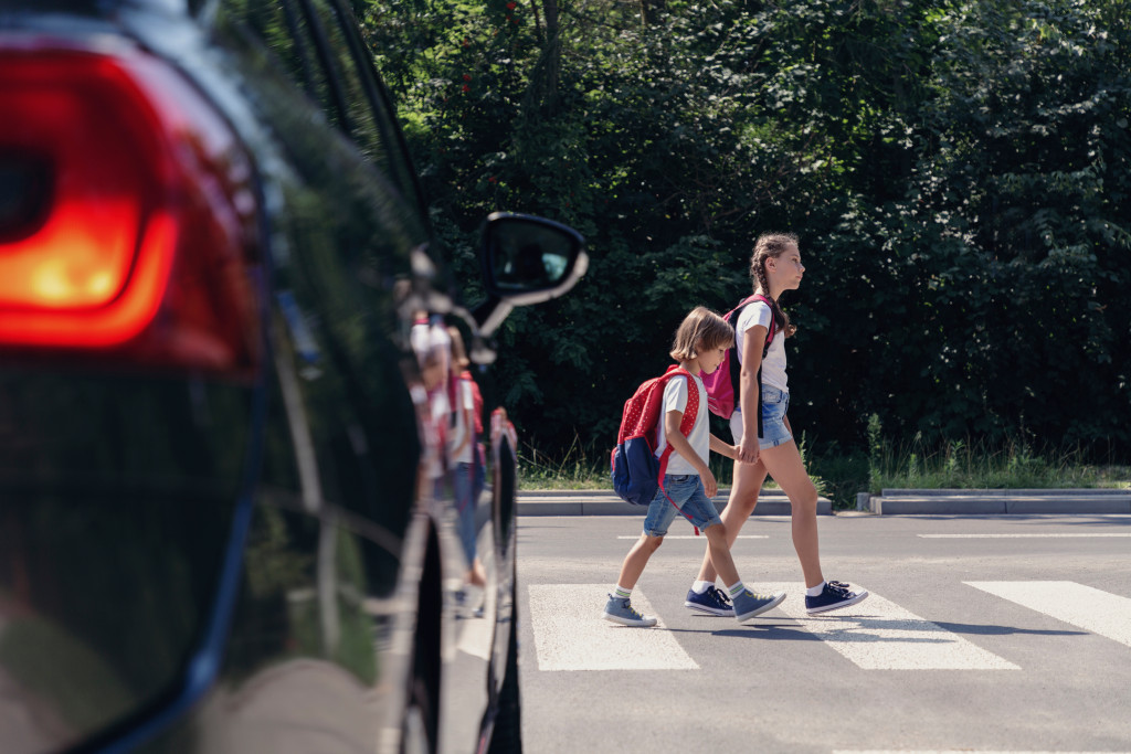 Two young kids cross the pedestrian lane while a car stops