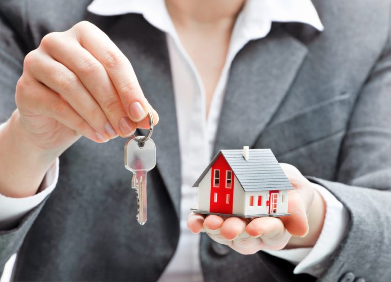 female real estate agent holding house key and model house in another hand